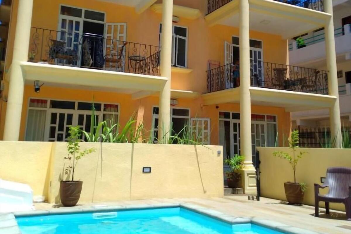 A multi-story building with balconies, a swimming pool, and potted plants.