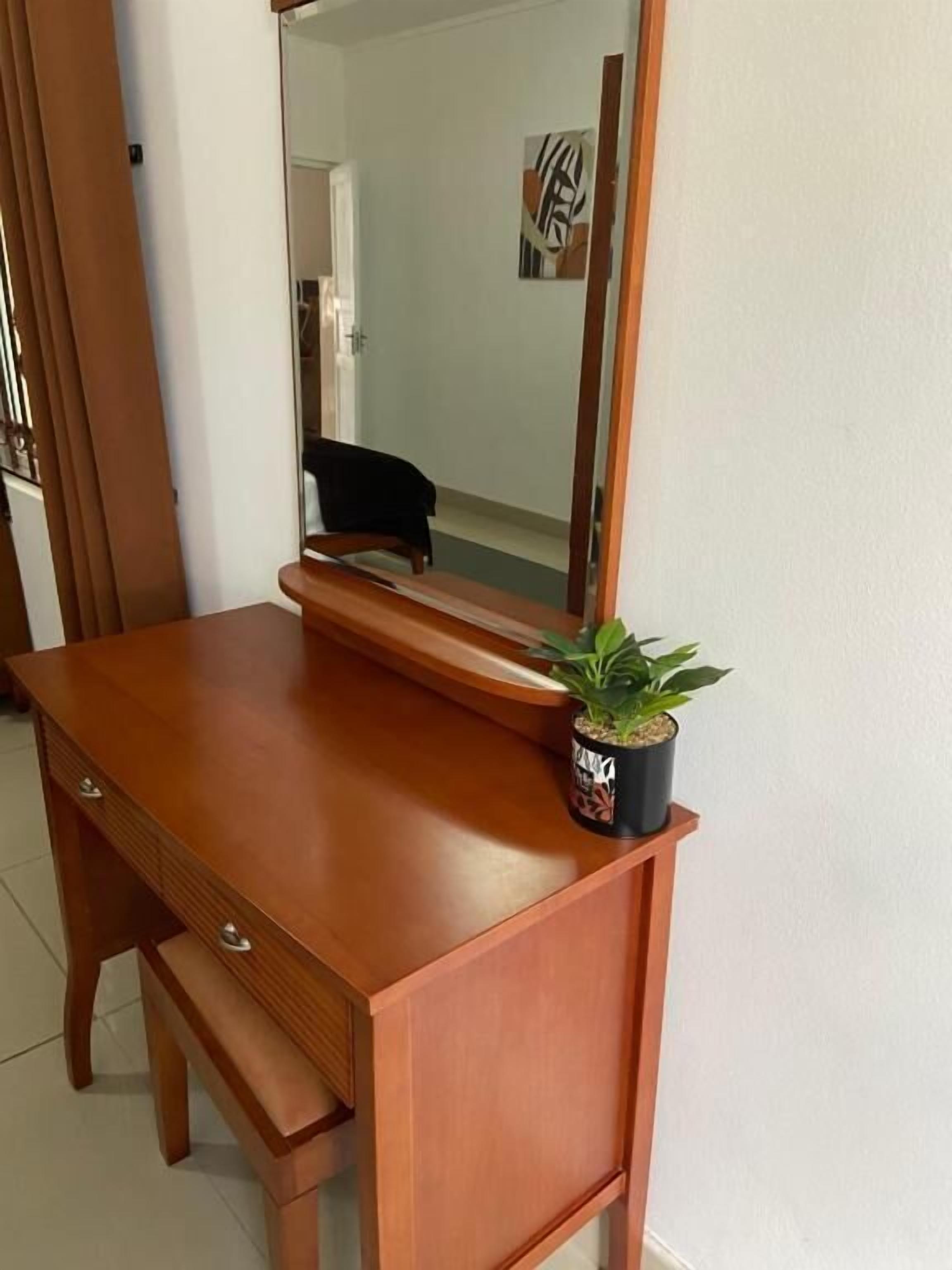 Et træskrivebord med en skuffe, et spejl og en potteplante.