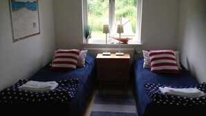 A room with two beds, each with a star-patterned bedspread, a nightstand with lamps, a window with a view of greenery, and a painting on the wall. - Systrarna på Kivik (Kivik)