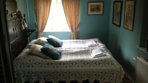 A room with a bed, curtains, a radiator, and framed pictures on the wall. - Systrarna på Kivik (Kivik)