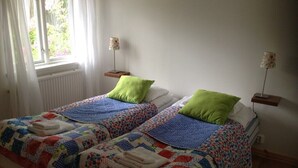 A double bed with a colorful quilt, two bedside tables with lamps, and a window with curtains. - Systrarna på Kivik (Kivik)