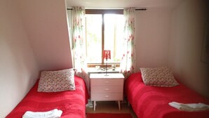 A small room with two single beds, a nightstand, a window with curtains, and a red carpet. - Systrarna på Kivik (Kivik)