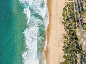 Eine Vogelperspektive zeigt einen Strand mit Wellen, einen Parkplatz und viel Grün.