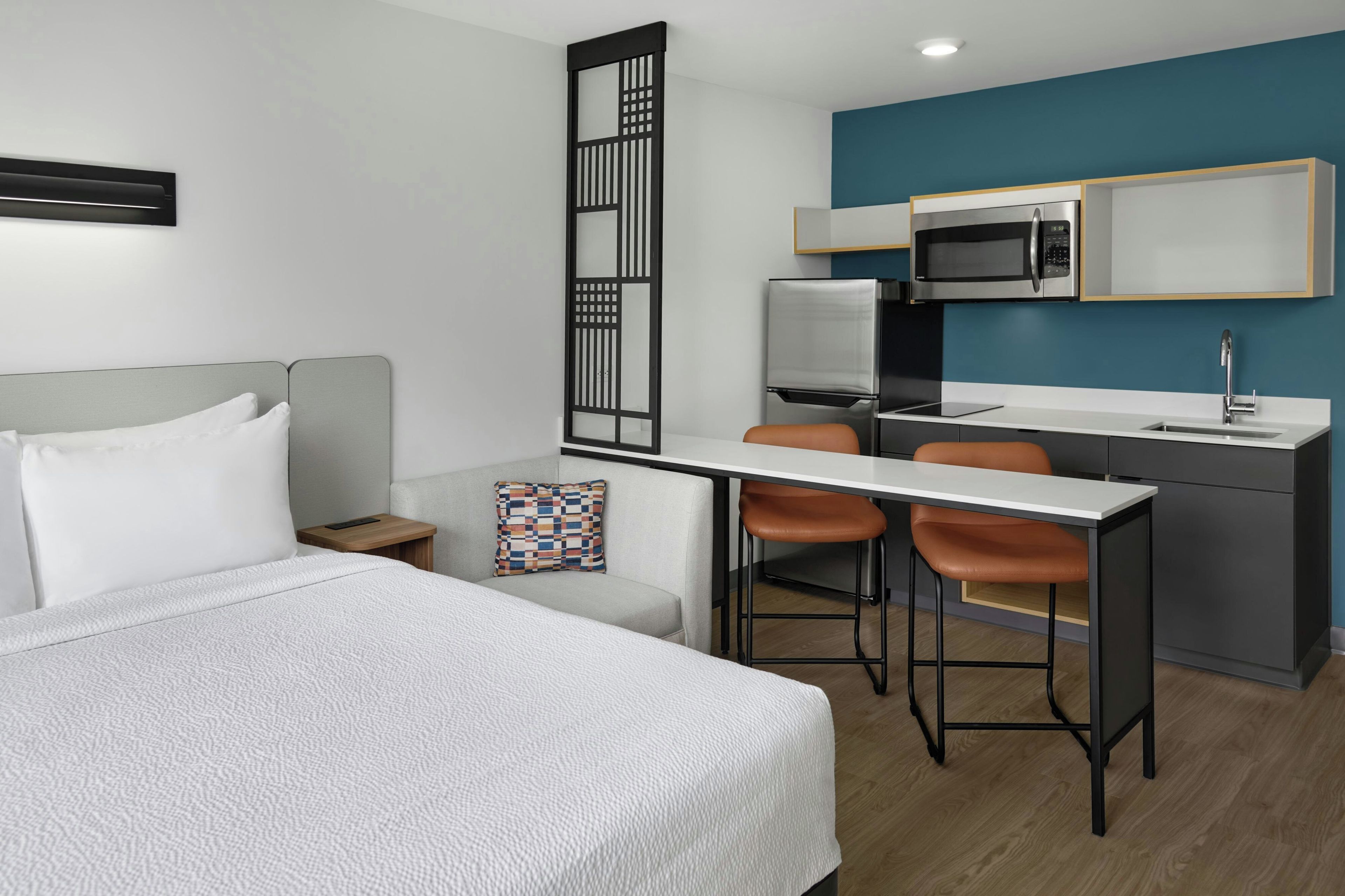 Habitación de hotel moderna con cama, escritorio, dos sillas, microondas y lavamanos.