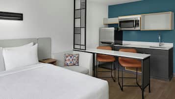 Habitación de hotel moderna con cama, escritorio, dos sillas, microondas y lavamanos.
