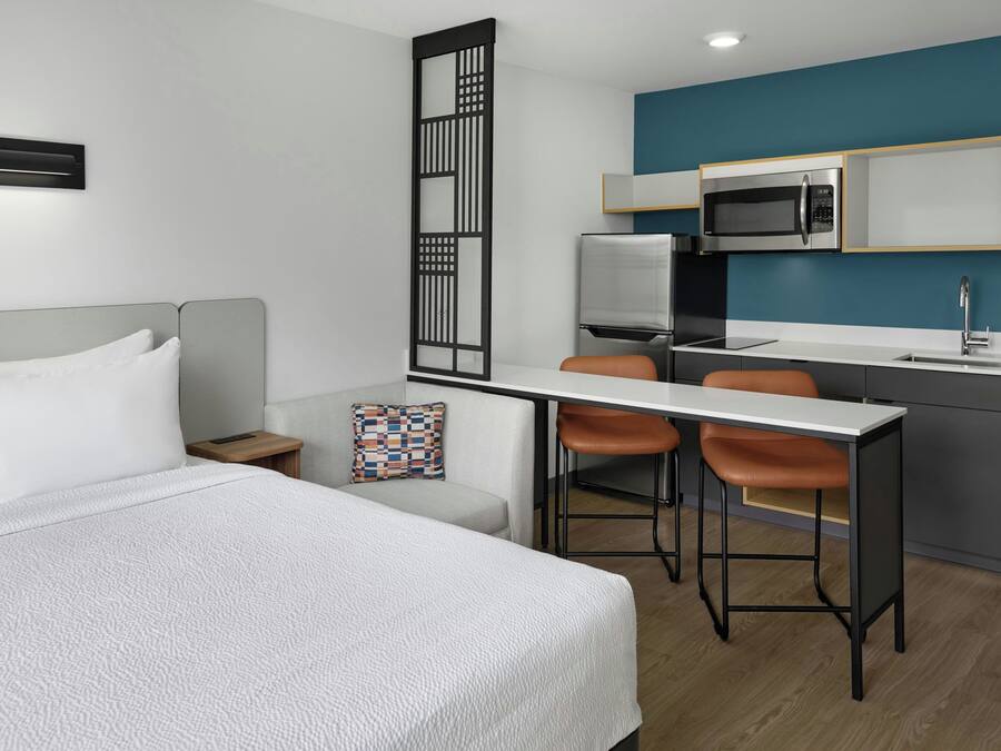 Habitación de hotel moderna con cama, escritorio, dos sillas, microondas y lavamanos.