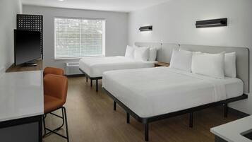 A hotel room with two beds, a desk, a chair, and a window with blinds.