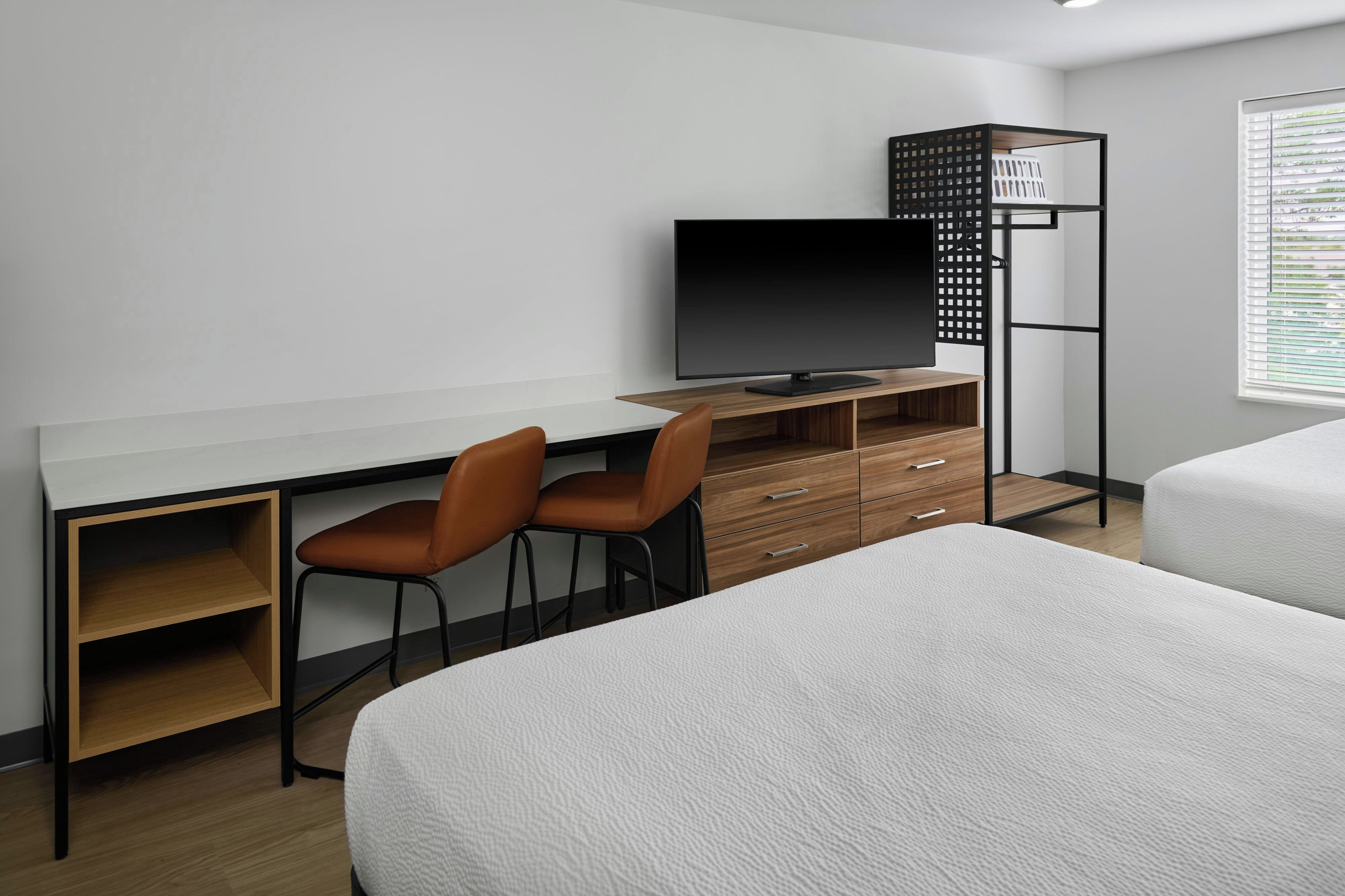A modern hotel room with a desk, two chairs, a TV, a wardrobe, and two beds.