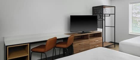 A modern hotel room with a desk, two chairs, a TV, a wardrobe, and two beds.