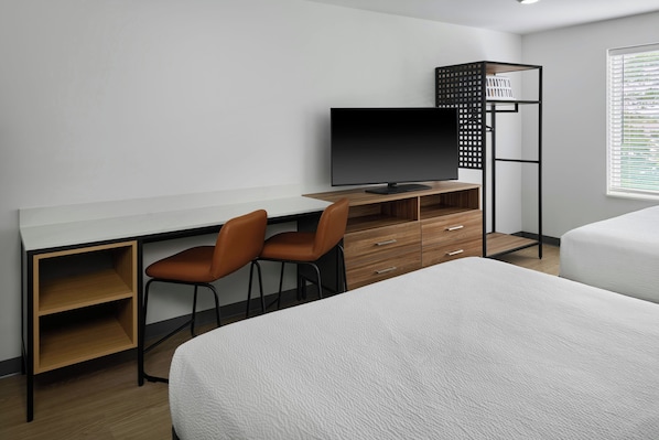 Una habitación de hotel moderna con escritorio, dos sillas, televisor, armario y dos camas.
