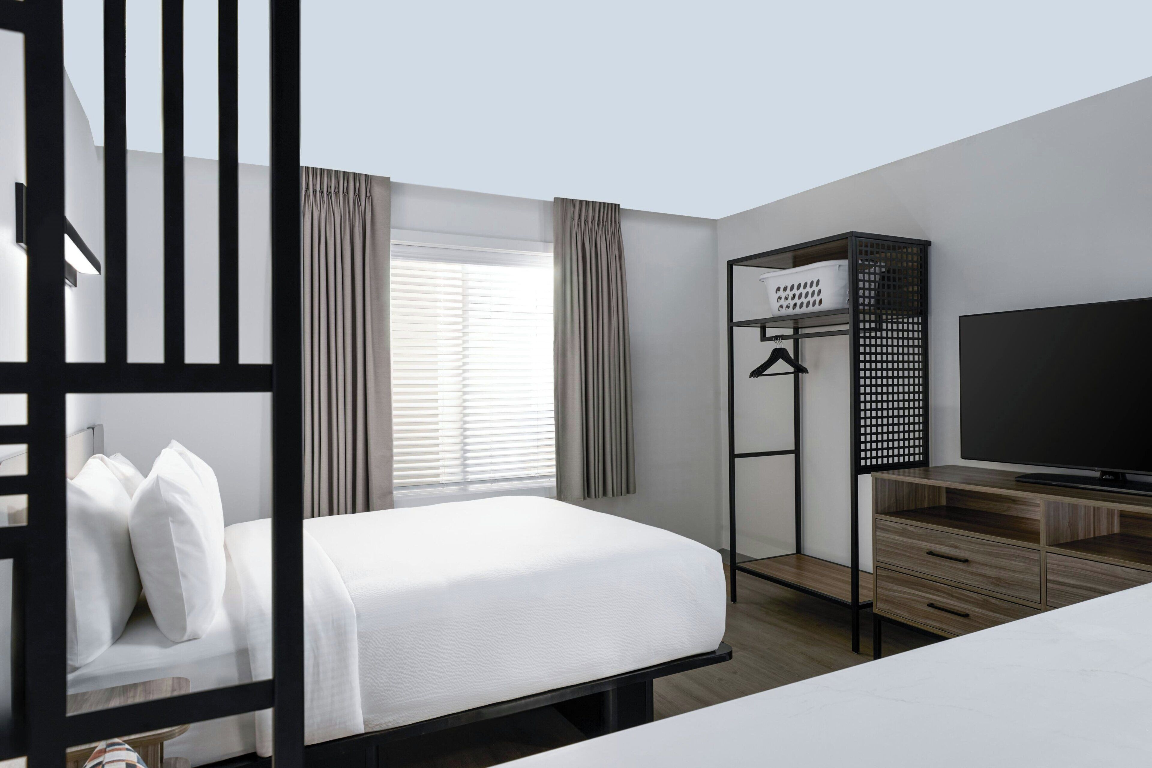 A hotel room with a bed, a TV, a desk with a computer, and a wardrobe.