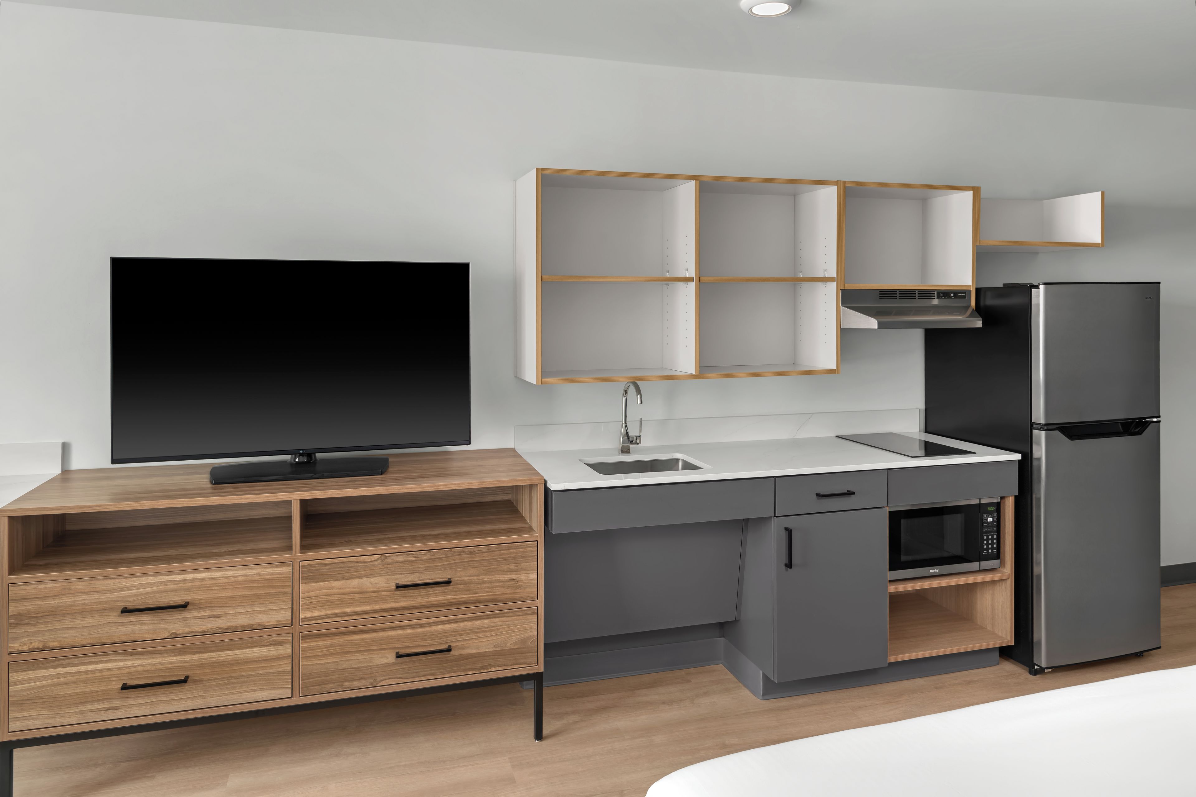 Una cocina moderna con televisor integrado, microondas, refrigerador y un mueble de madera con cajones.