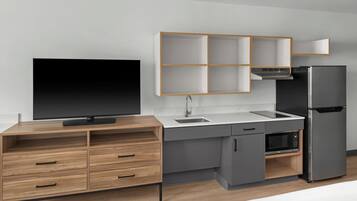 Una cocina moderna con televisor integrado, microondas, refrigerador y un mueble de madera con cajones.