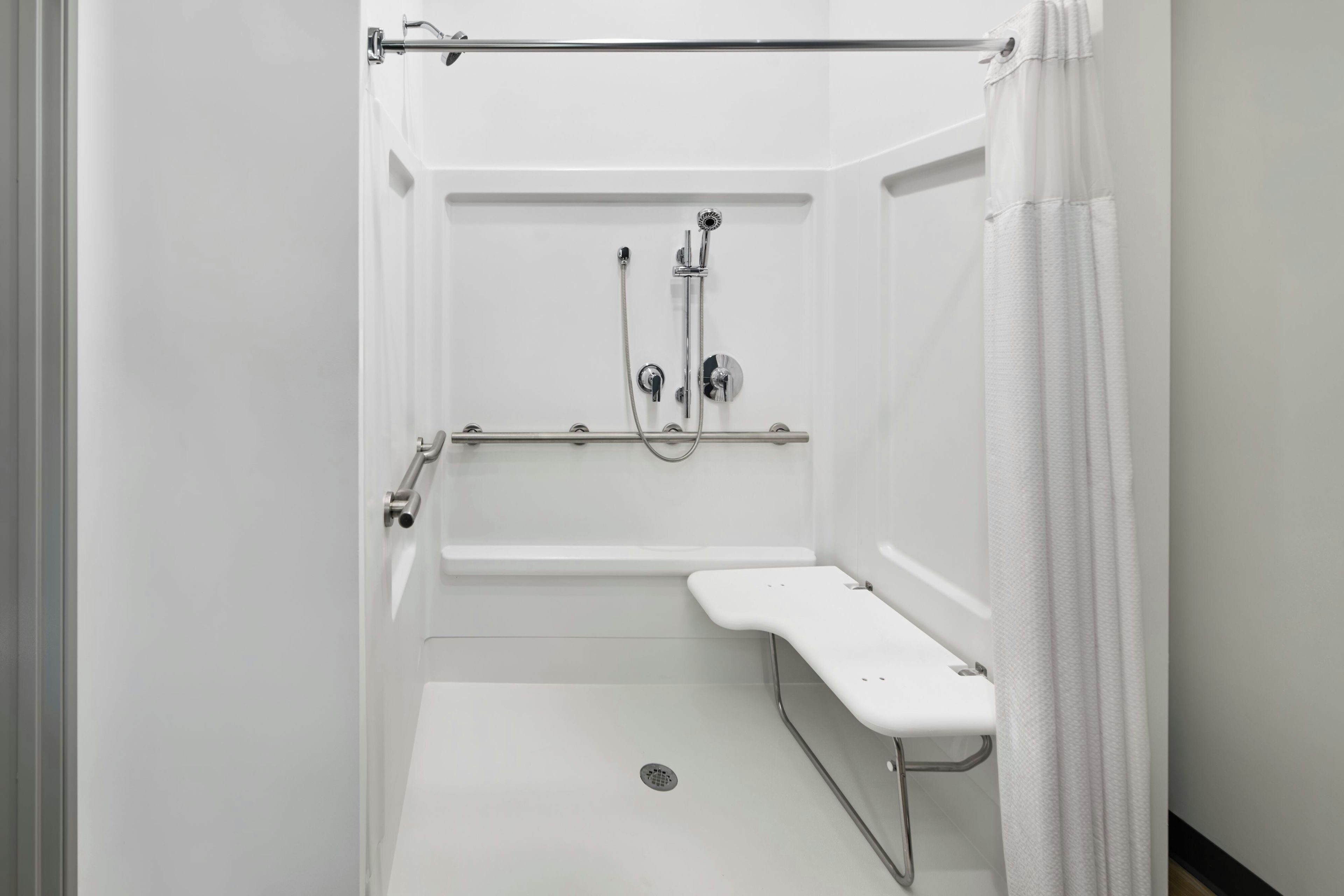 Eine weiße, barrierefreie Duschkabine mit Haltegriff, Duschbrause und Armatur.