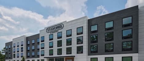 Een modern hotel met een bord waarop 'STUDIOS BY MARRIOTT' staat en een parkeerplaats met duidelijke parkeerplaatsen.