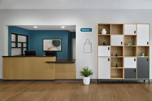 A reception desk with a computer, a wall-mounted sign labeled 'Deliveries', and a shelving unit with plants. - StudioRes by Marriott Wilmington (Wilmington)
