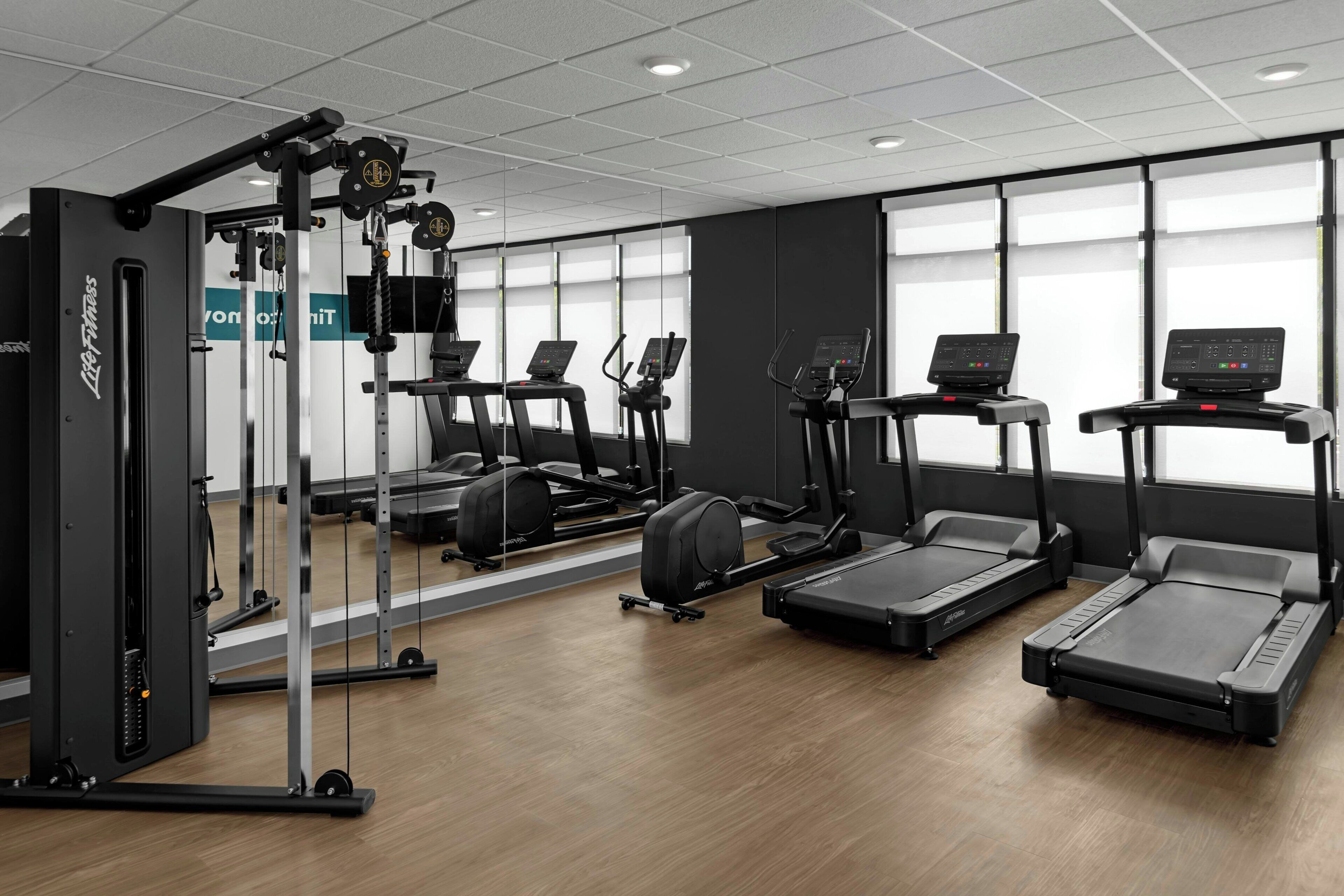 Ein Fitnessstudio mit Laufbändern, Krafttrainingsgeräten und einer Spiegelwand.