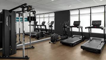 Ein Fitnessstudio mit Laufbändern, Krafttrainingsgeräten und einer Spiegelwand.