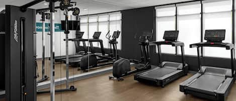 Un gimnasio con máquinas de cardio, equipo de entrenamiento de pesas y un espejo grande.