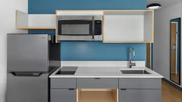 Una cocina compacta con microondas integrado, refrigerador de acero inoxidable y pileta con grifo moderno.