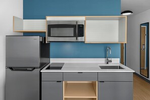 A compact kitchen with a built-in microwave, a stainless steel refrigerator, and a sink with a modern faucet. - StudioRes by Marriott™ Fayetteville West near Fort Bragg (Fayetteville)