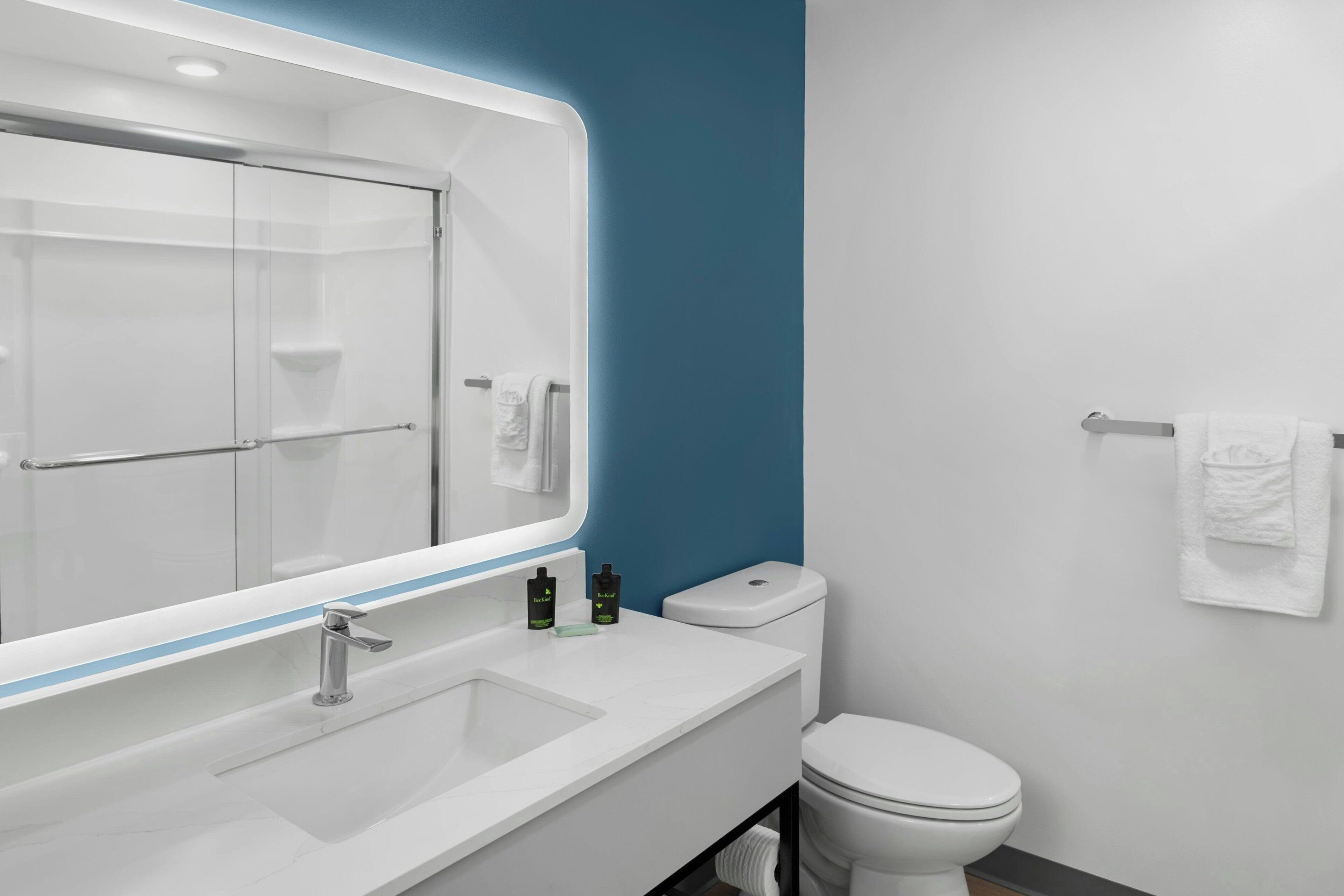 A modern bathroom with a white sink, a mirror, a toilet, and a towel rack.