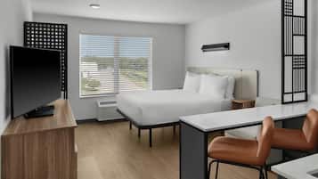 Habitación de hotel moderna con cama, escritorio, silla, televisor y ventana con persianas.