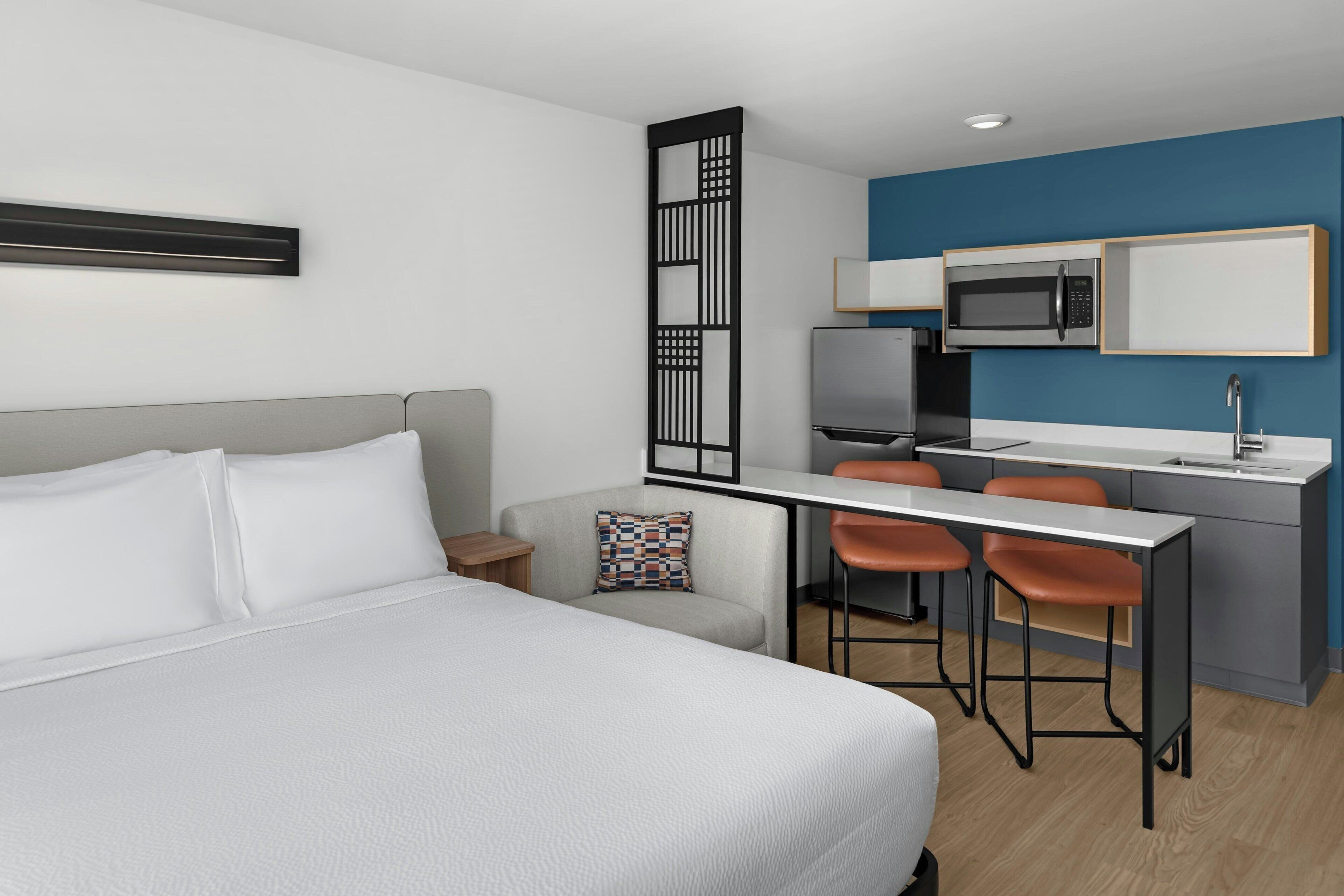 A hotel room with a bed, a desk, a microwave, and a refrigerator.