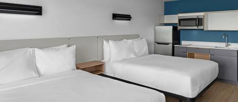 Quarto de hotel com duas camas, uma cozinha compacta e banheiro.