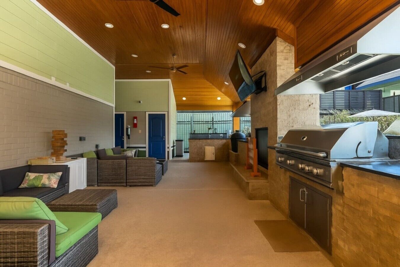Een moderne keuken met een ingebouwde grill, een zithoek met banken en een zichtbare deur naar een andere kamer.