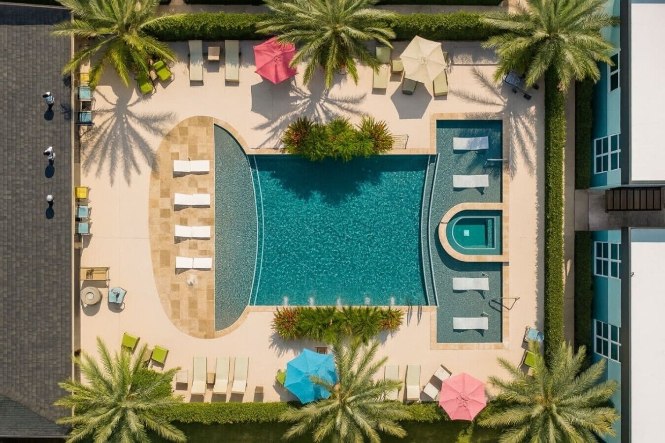 An aerial view of a resort with a central swimming pool, sun loungers, and palm trees.