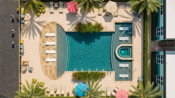 An aerial view of a resort with a central swimming pool, sun loungers, and palm trees.