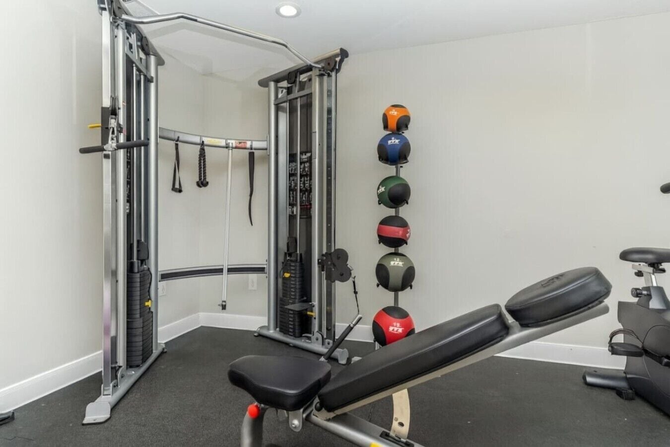 A gym with a bench, weightlifting equipment, and medicine balls on the wall.