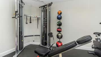A gym with a bench, weightlifting equipment, and medicine balls on the wall.