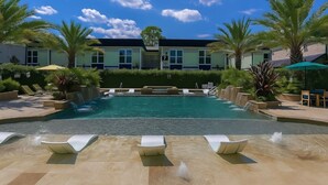 Uma piscina com espreguiçadeiras, palmeiras e um edifício com janelas ao fundo.