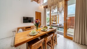 A dining area with a wooden table, chairs, a TV, and a view of a pool. - Sunset Heaven C6 Villa (Denpasar)