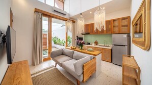 A modern kitchen with wooden cabinets, a built-in fridge, and a dining area with a sofa and table. - Sunset Heaven C6 Villa (Denpasar)