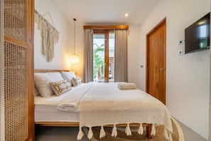 Ein Schlafzimmer mit einem Bett, einem Fernseher, einem Fenster mit Vorhängen und einer Pflanze.