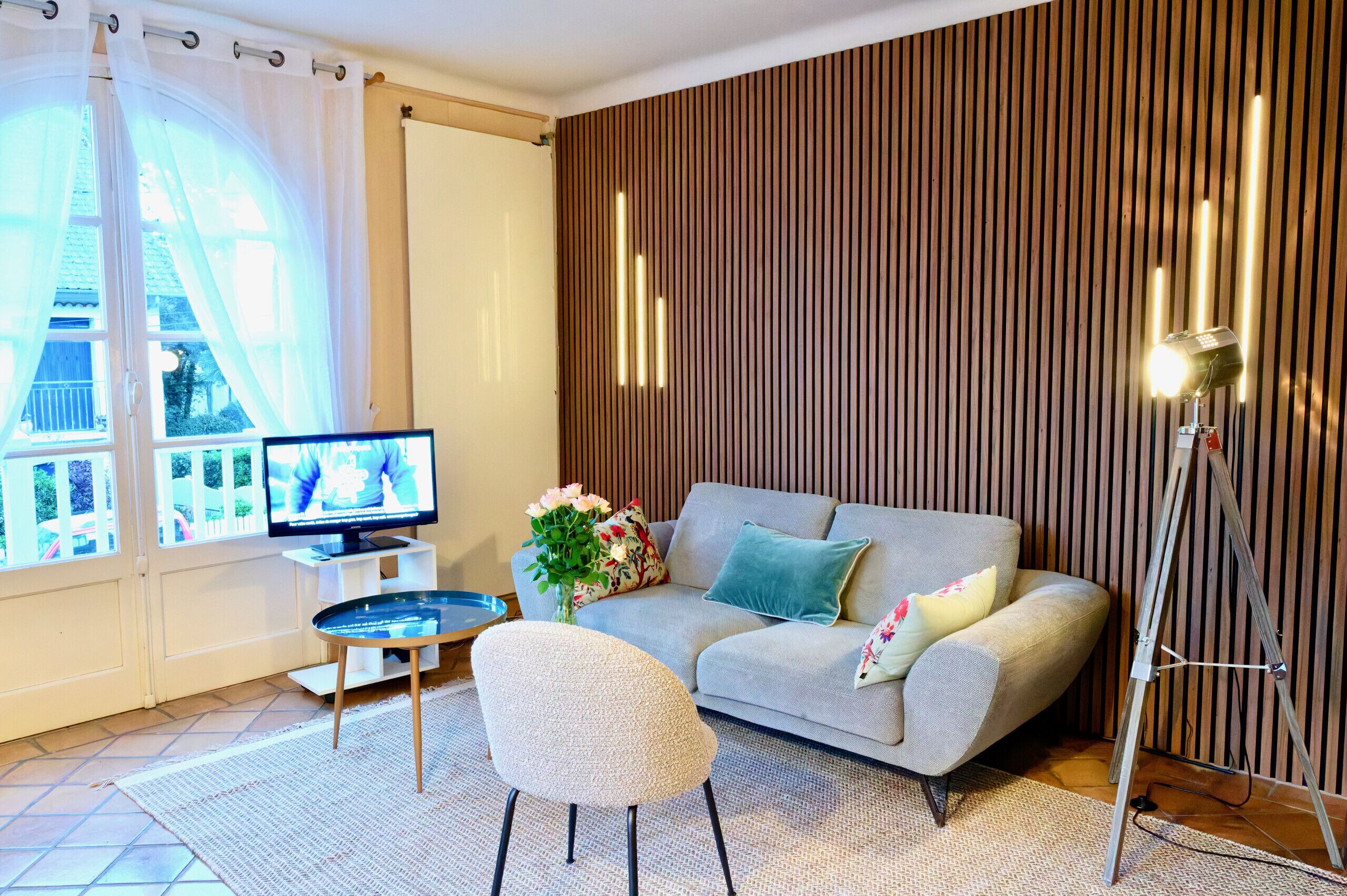 Un salon moderne comprenant un canapé, un téléviseur, une petite table et un lampadaire.