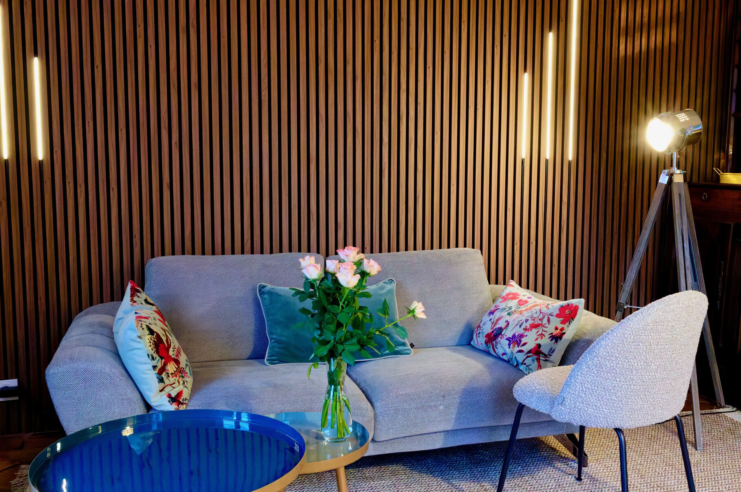 A modern living room with a sofa, a chair, a glass coffee table, a vase with flowers, and a lamp.