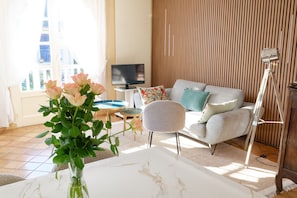 Ein Wohnzimmer mit einer Couch, einem Fernseher, einer Blumenvase und einer Holzwand.