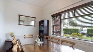 Un comedor con una mesa y sillas de madera, una estantería, un espejo y una ventana con persianas.