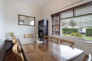 A dining area with a wooden table and chairs, a bookshelf, a mirror, and a window with blinds. - Stylish 1BR Vaucluse Escape | Near Shops & CBD (Vaucluse)