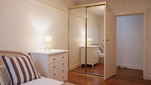 Un dormitorio con cama, mesita de noche, lámpara y armario con espejo.