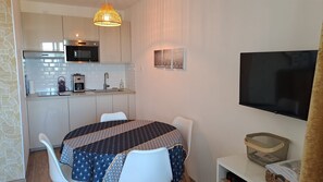 Een compacte keuken met moderne apparaten, een eethoek met een tafelkleed met een patroon, en een flatscreen televisie aan de muur.