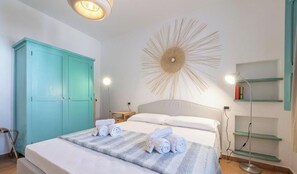 Ein Schlafzimmer mit einem Bett, einem türkisblauen Kleiderschrank, einem Wandbild und Nachttischlampen sowie einer Stehlampe.