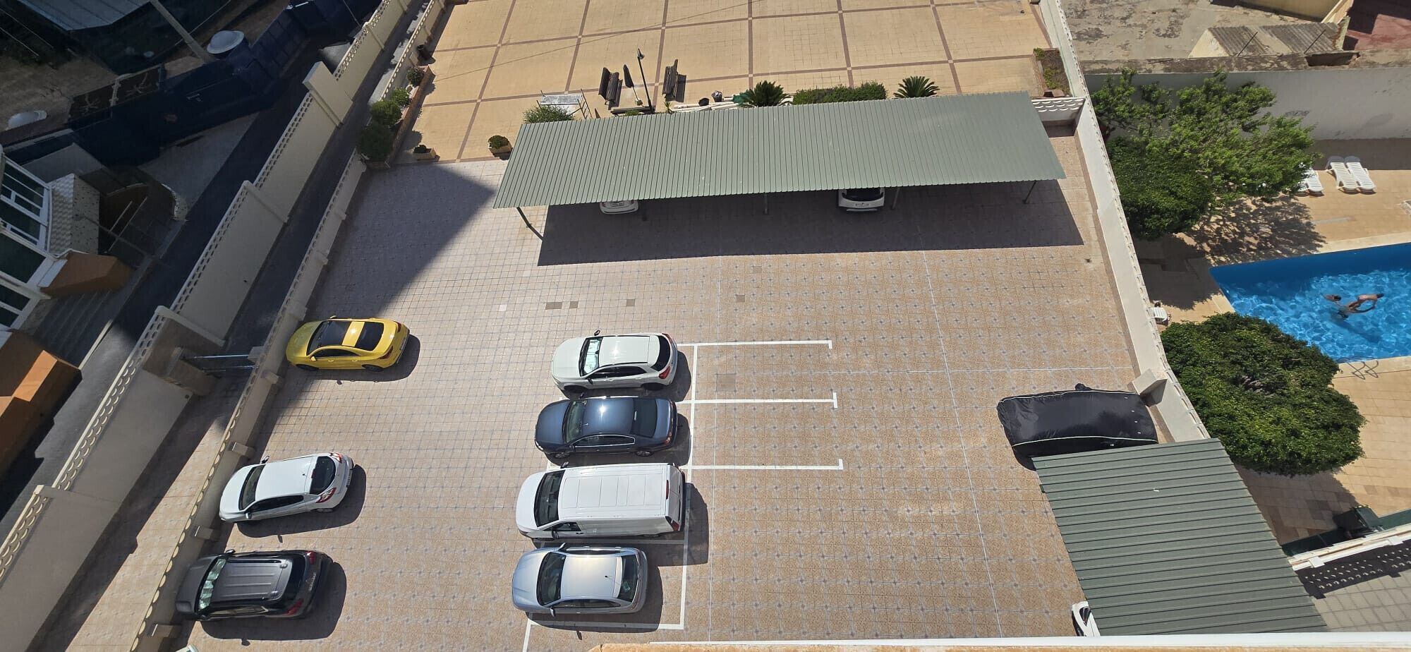 Eine Vogelperspektive auf einen Parkplatz mit mehreren Autos, einem Schwimmbad und einem Gebäude mit einer Gründachfläche.