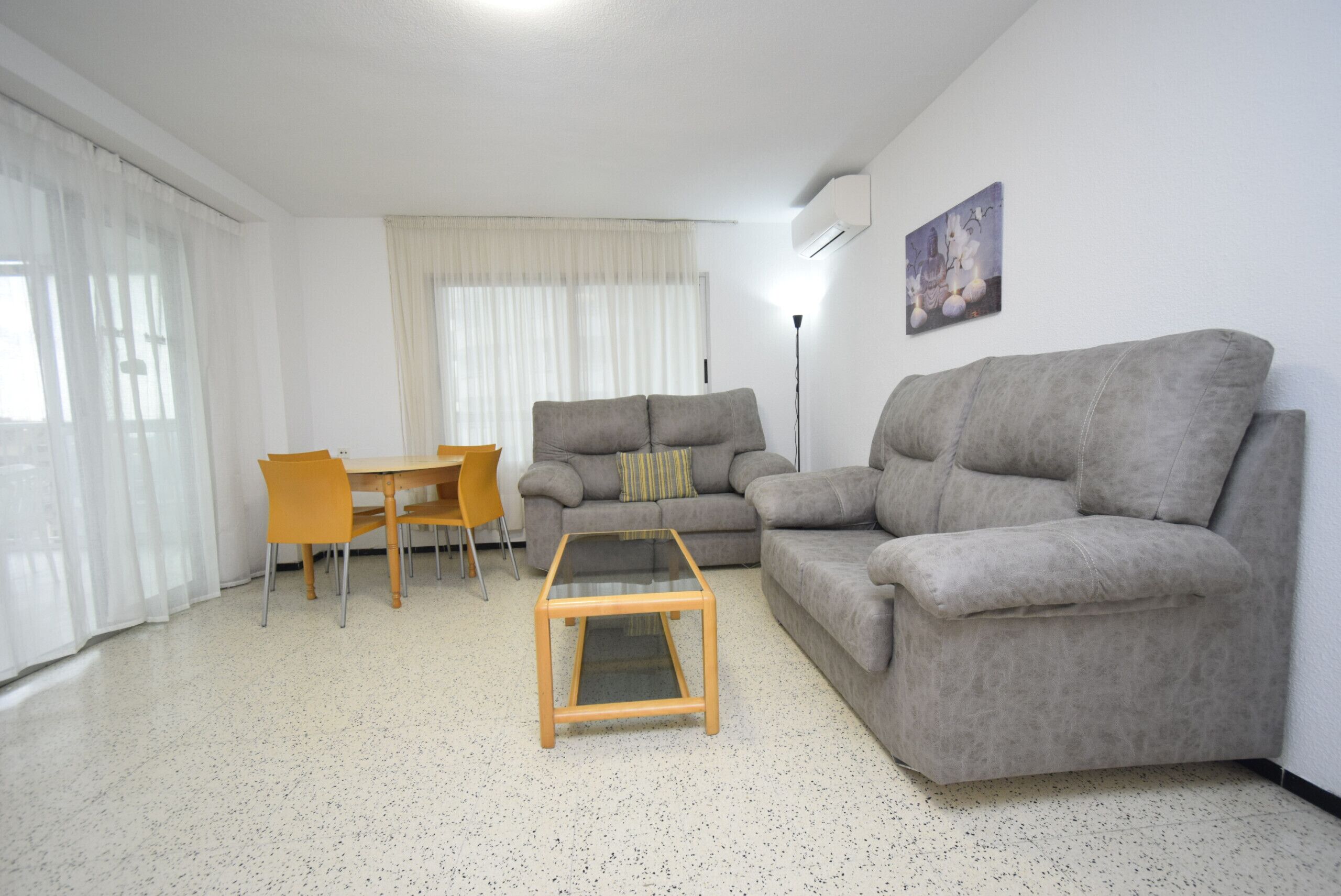Un salon avec un canapé gris, une table basse en verre, un fauteuil jaune et une table à manger.