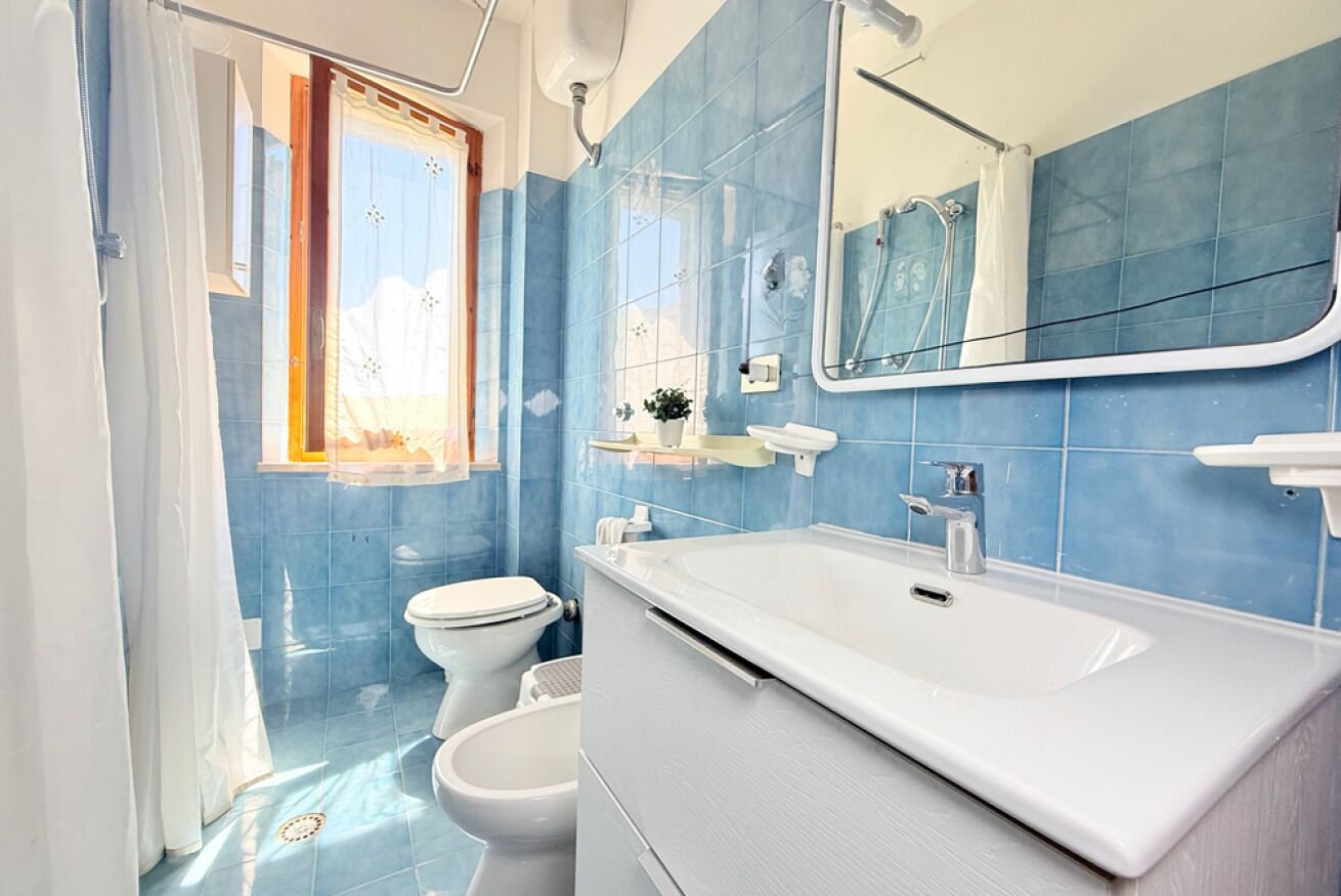 Un bagno con piastrelle blu, un lavandino bianco, uno specchio e un water.