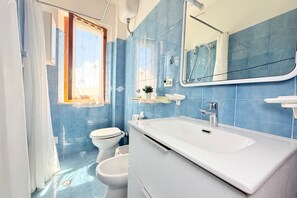 Ein Badezimmer mit blauen Fliesen, einem weißen Waschbecken, einem Spiegel und einer Toilette.
